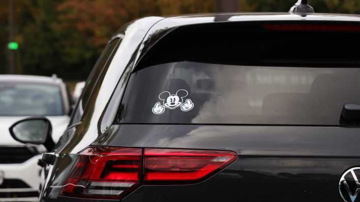 Ein Mickey-Mouse-Aufkleber mit Mittelfinger-Geste ist auf der Heckscheibe eines VW Golf zu sehen.