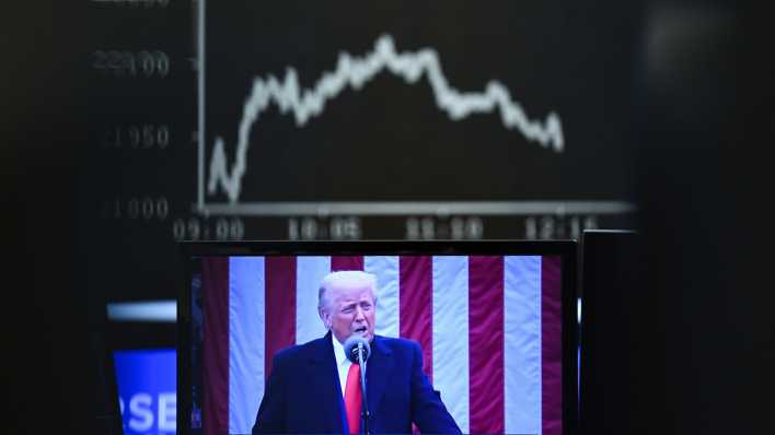 Hinter einem Fernsehmonitor, auf dem US-Präsident Donald Trump zu sehen ist, zeigt die Anzeigetafel mit der Dax-Kurve fallende Kurse.