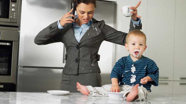 Eine Mutter steht mit beflecktem Blazer in der Küche, während das Kind im Essen manscht (Bild. picture alliance/Carte Blanche/Frank and Helena)