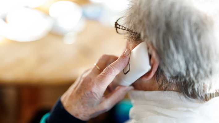 Eine alte Dame führt ein Gespräch an einem Festnetztelefon.