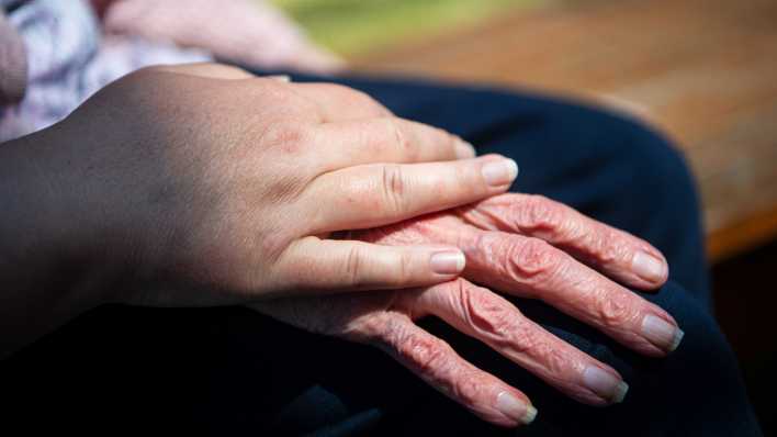 Die Hand einer Pflegefachkraft liegt auf der Hand einer Bewohnerin des Seniorenheims.