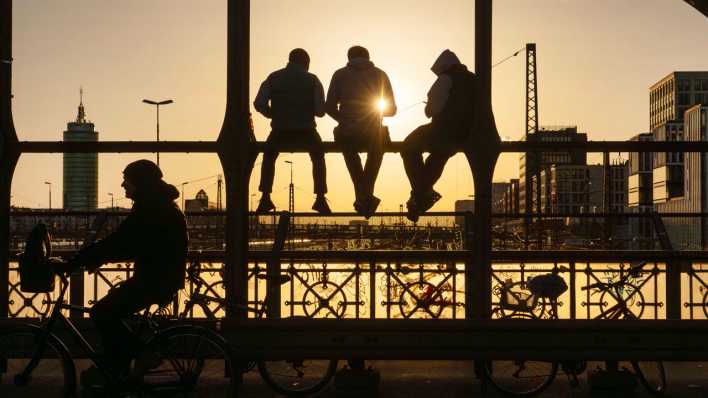 Jugendliche sitzen im Sonnenuntergang auf einer Brücke.
