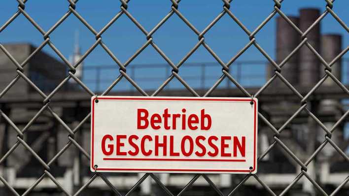 Symbol Wirtschaftskrise: Hinweisschild an Maschendrahtzaun vor Betriebsgelände: Betrieb geschlossen (Bild: IMAGO/IlluPics)