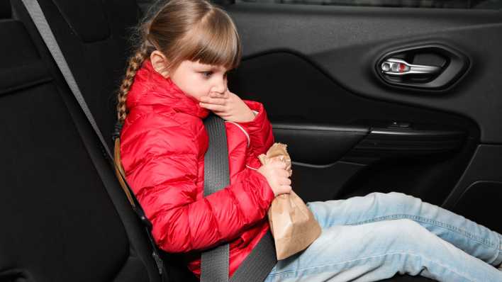 Ein kleines Mädchen sitzt im Auto und leidet an Übelkeit.