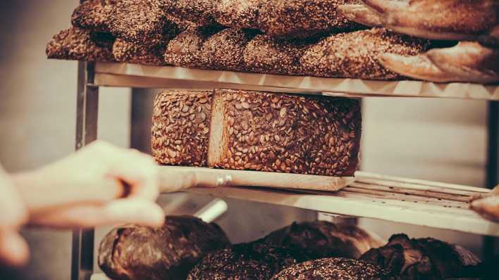 Ein Bäcker legt frisch gebackenes Vollkornbrot in ein Verkaufsregal.