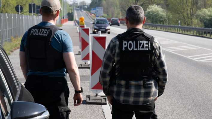 Zwei Polizisten stehen am Grenzübergang am Straßenrand und beobachten den Verkehr.
