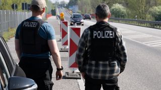 Zwei Polizisten stehen am Grenzübergang am Straßenrand und beobachten den Verkehr.