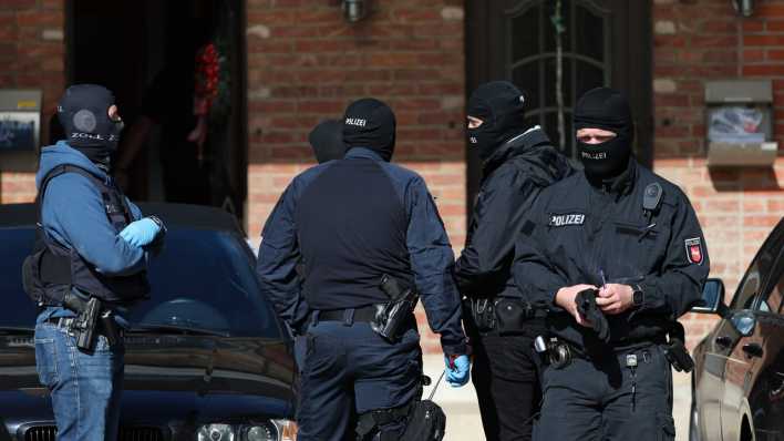 Polizisten stehen bei einer Razzia vor einem Haus.