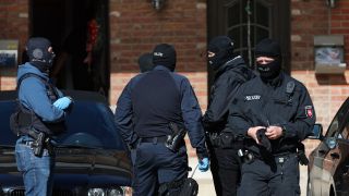Polizisten stehen bei einer Razzia vor einem Haus.