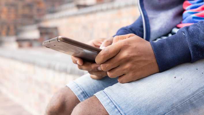 Einn Jugendlicher sitzt auf einer Treppe und tippt auf sein Smartphone.