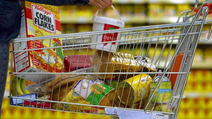 Eine Kundin legt in einem Supermarkt einen Joghurt-Becher in ihren mit Lebensmitteln gefüllten Einkaufswagen