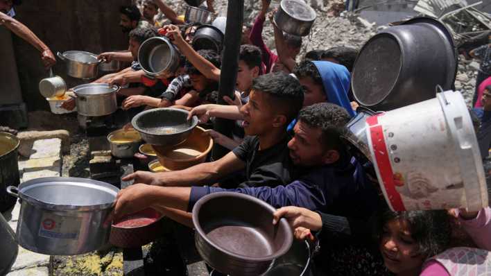 Menschen im Gazastreifen warten mit Töpfen in den Händen auf Nahrungsmittel an einer Gemeinschaftsküche in Jabalia.