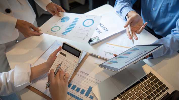 EIn Team diskutiert über Finanzanalysen mit Balken- und Tortendiagrammen (Bild: picture alliance / Zoonar / Natee Meepian)