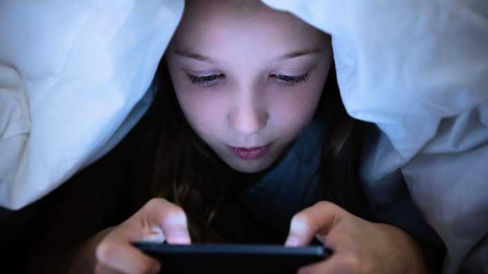 Mädchen benutzt unter ihrer Decke ihr Smartphone