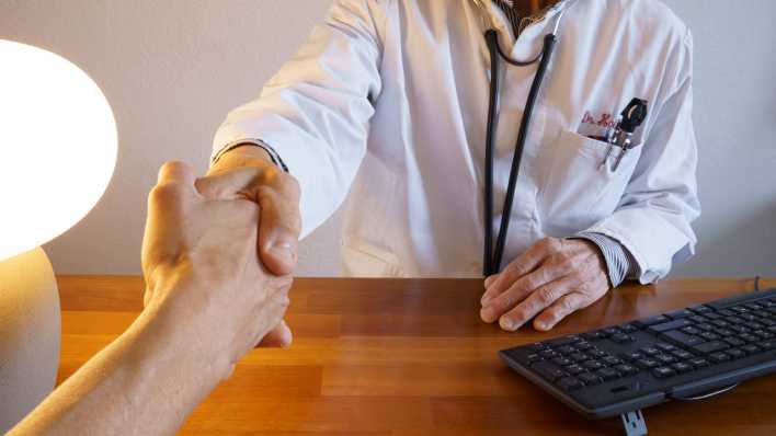 Ein Arzt im Laborkittel begrüßt einen Patienten mit Handschlag.