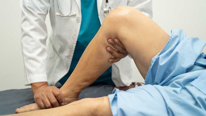 Arzt untersucht das Knie einer älteren Frau