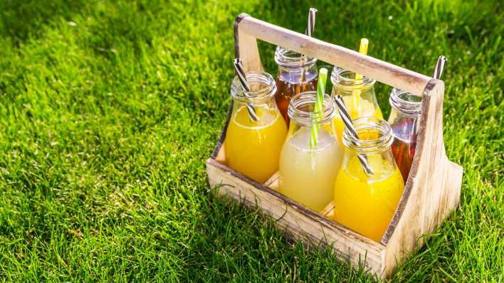 Sortiment von Limonade und Eistee in Flaschen in einem Holzregal im Gras