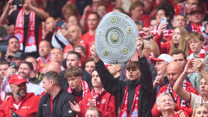 Ein FC Bayern-Fan hält eine Meisterschale hoch