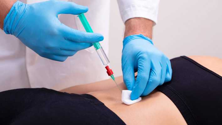 Symbolfoto: Ein Arzt setzt eine Spritze auf dem Rücken einer Patientin.