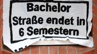 Ein Transparent mit der Aufschrift "Bachelor: Straße endet in 6 Semestern" hängt vor einem Hörsaal (Bild: dpa)