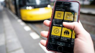 Eine Frau benutzt vor einer einfahrenden Tram die App der Berliner Verkehrsbetriebe (BVG), um sich online eine Fahrkarte zu kaufen. (Quelle: dpa/Fabian Sommer)